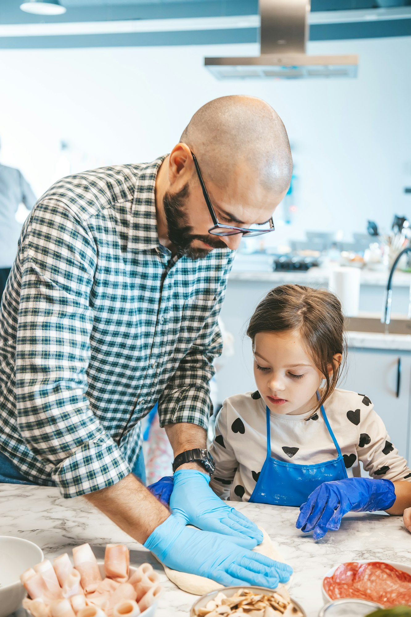 A little girl and her father working together in a modern kitchen, as they prepare a homemade pizza